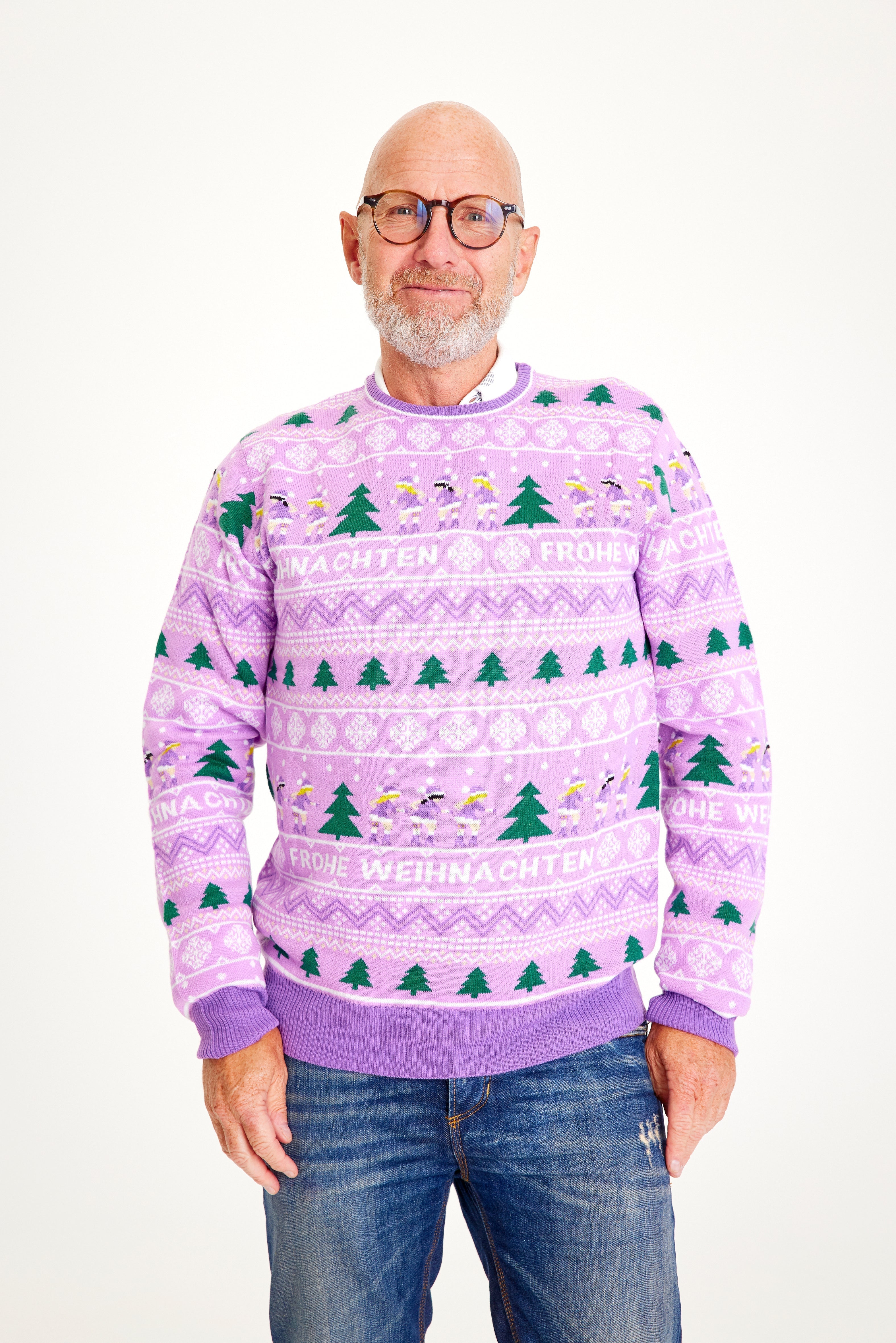 Een poserende man die een paarse kersttrui draagt met kerstbomen erop.